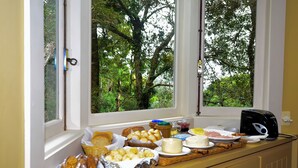 Un buffet de petit-déjeuner proposant une variété de pains, de fromages et de viennoiseries, le tout disposé sur un comptoir près d’une fenêtre donnant sur les arbres.