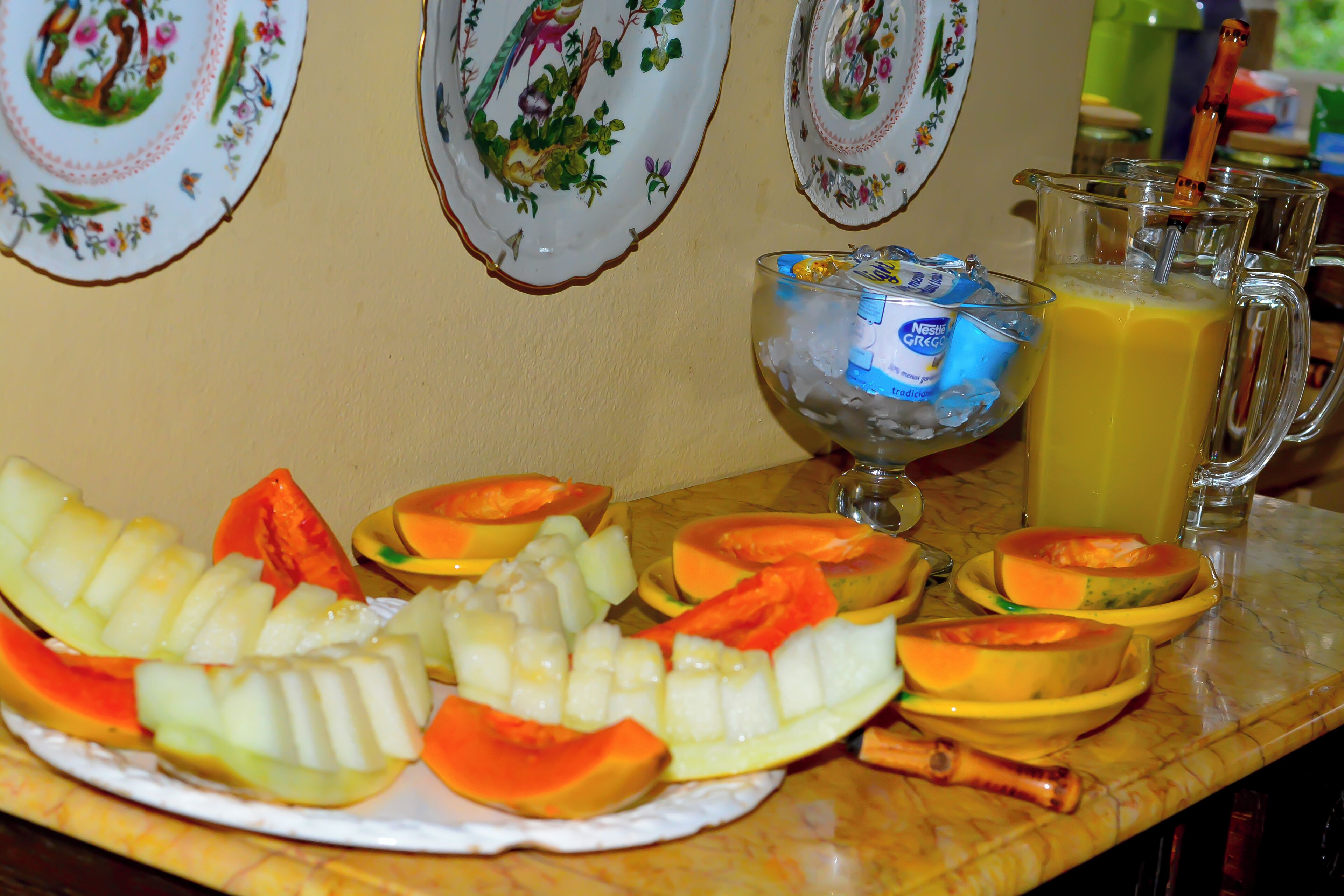 Una mesa con una bandeja de frutas, una jarra de jugo y platos decorativos.