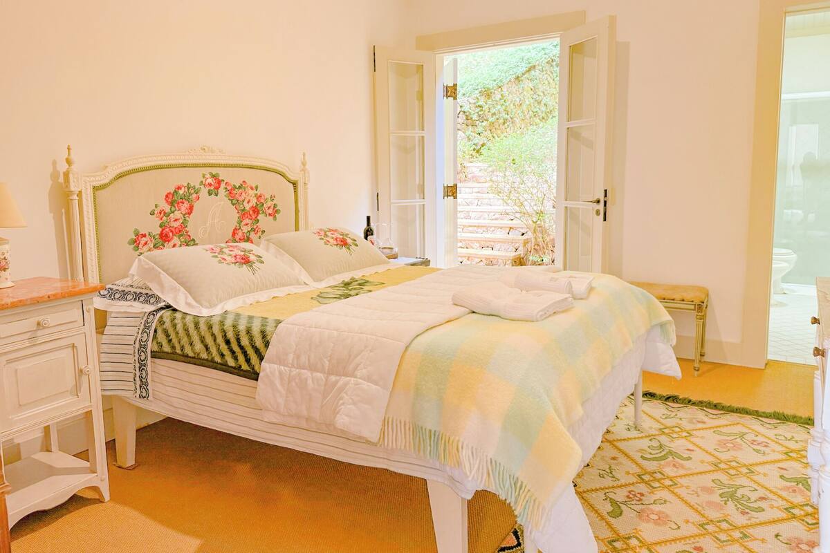 Un dormitorio con cama, mesita de noche, cómoda y ventana con vista a follaje.
