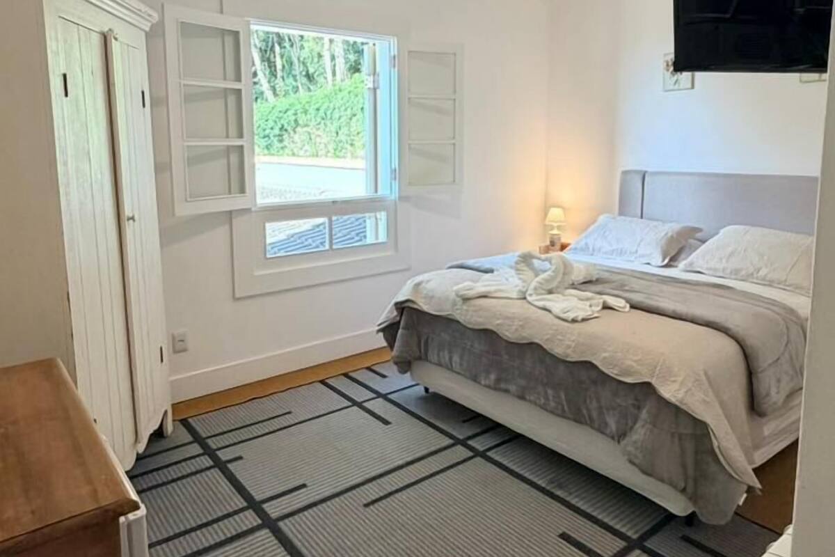 Un dormitorio con cama, televisión montada en la pared, ventana y radiador.