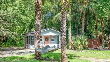 A small house with a porch, surrounded by lush greenery and palm trees.