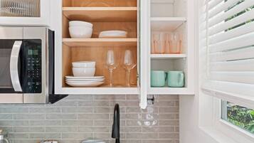 A kitchen with a microwave, a cabinet with dishes and glasses, and a window with blinds.