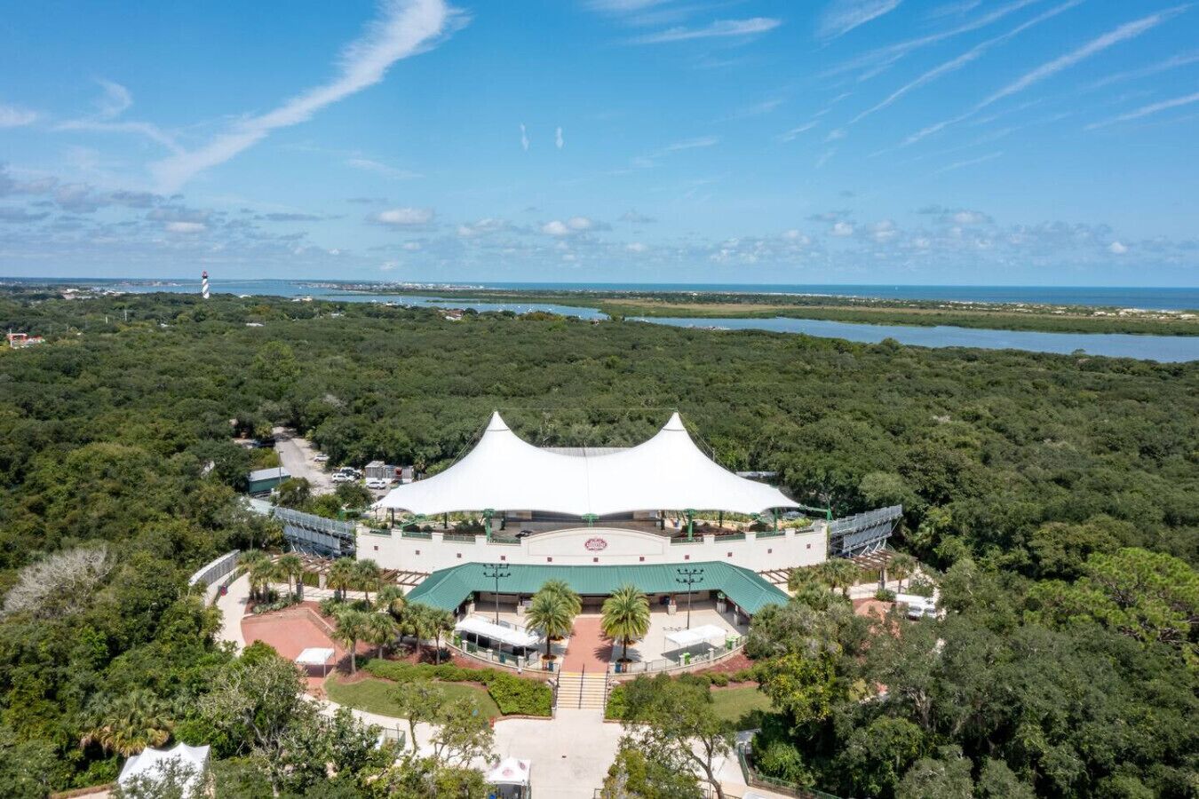 An aerial view of a large, white, tent-like structure surrounded by lush greenery and a body of water.