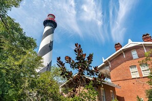 A lighthouse with a spiral design, a brick building with white windows, and surrounding greenery.