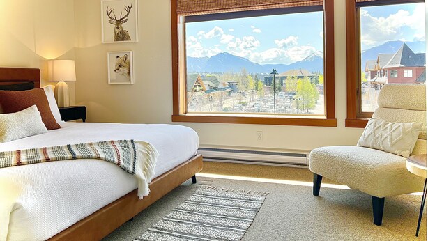 A hotel room with a bed, a chair, a view of mountains, and a cityscape. - Feel at Home after a Day of Adventures in this Family friendly Retreat! (Canmore)