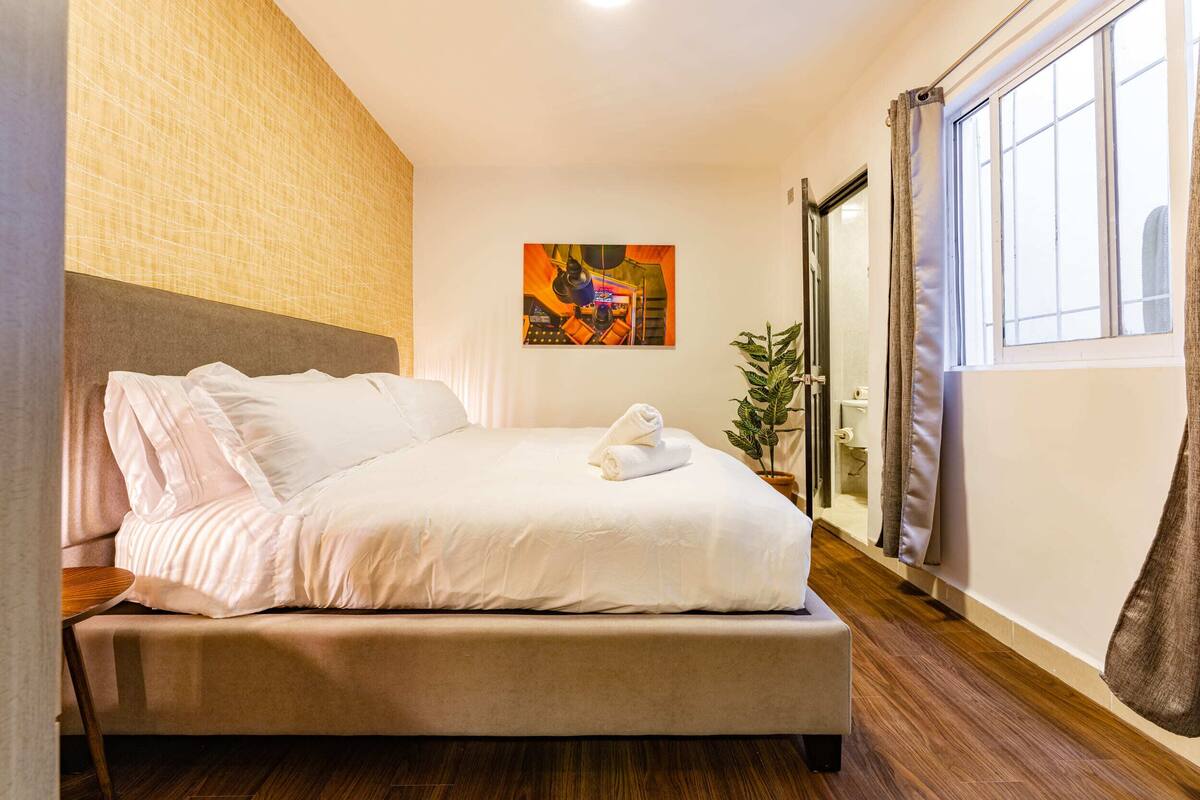 Un lit bien fait, avec des draps blancs, une tête de lit et un tableau accroché au mur.