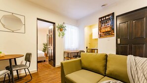 A living room with a green sofa, a dining table with chairs, a small kitchen area, and a door leading to another room. - Condesa Zamora Lofts by VH (Mexico City)