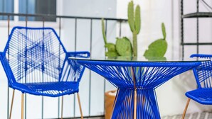 A glass-top table with blue wire chairs, a cactus, and a black railing in the background. - Condesa Zamora Lofts by VH (Mexico City)