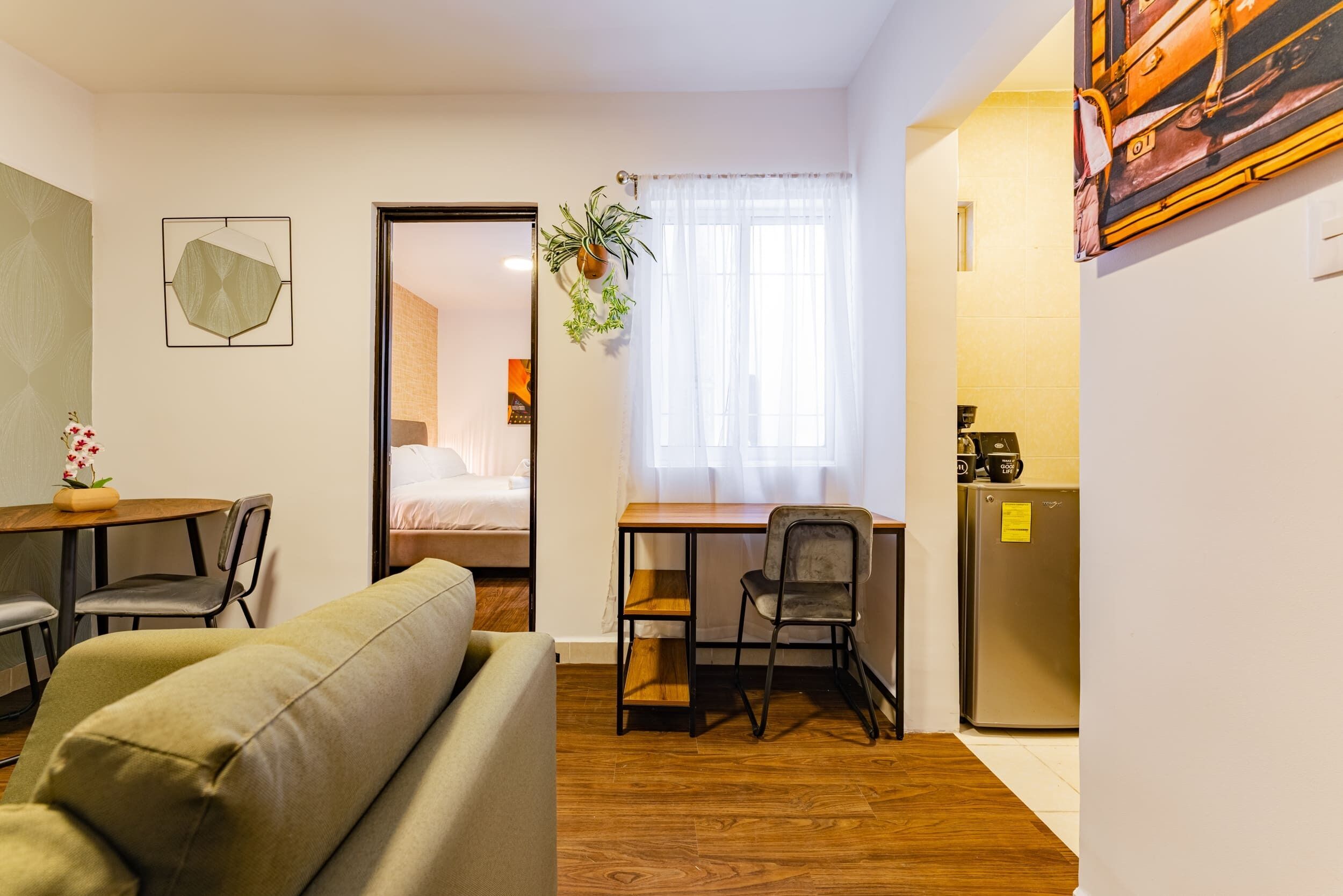 A compact living space with a sofa, a dining table with chairs, a small kitchen area, and a door leading to a bedroom.