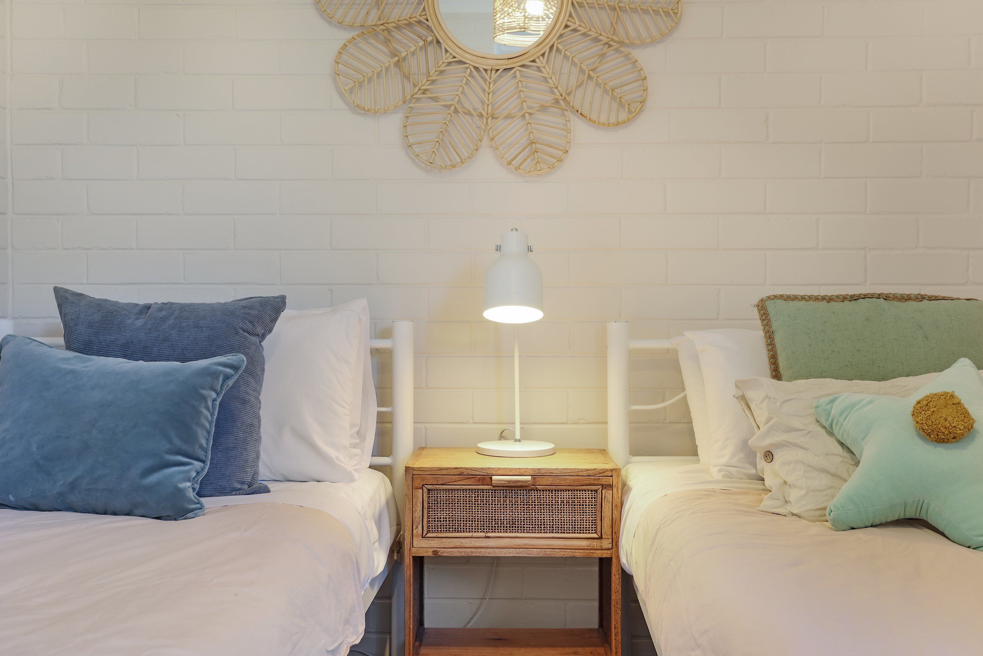 A bedroom with two beds, a bedside table with a lamp, and a decorative mirror on the wall.