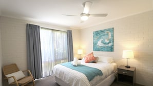 A bedroom with a large bed, two bedside lamps, a ceiling fan, a chair, and a window with curtains. - Poolside - Ground floor opposite pool (Merimbula)