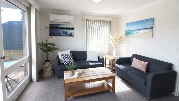 A living room with a dark blue sofa, a wooden coffee table, and a potted plant. - Poolside - Ground floor opposite pool (Merimbula)
