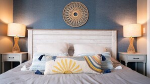 Una cama bien hecha con almohadones decorativos, un cabecero de madera y dos lámparas de noche en mesitas a juego.