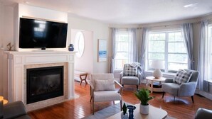Una sala de estar con chimenea, un televisor de pantalla plana, dos sillones, una mesa de centro y una mesita de noche con lámpara.