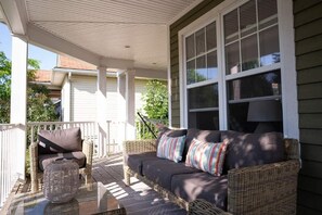A covered porch with wicker furniture, including a sofa and chairs, and a glass table.