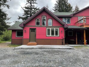 Ein zweigeschossiges Haus mit roter Fassade, einer Veranda und einer Auffahrt mit Kies.