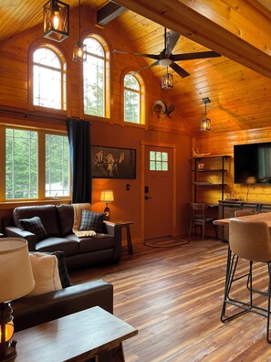 Ein gemütliches Blockhaus-Interieur mit Holzwänden, einem Deckenventilator, einem Kamin, einem Essbereich und einem Wohnzimmer mit einer Couch und Lampen.