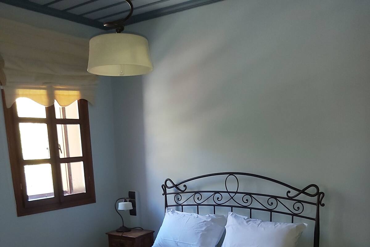Ein ordentlich bezogenes Bett mit weißen Leinen, einem Holzkopfende und einem Fenster mit Vorhängen.