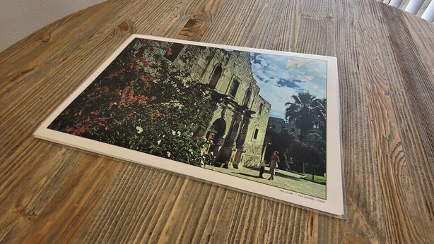 Een ronde houten tafel met een fotolijstje van een gebouw.