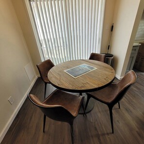 Una mesa de madera redonda con un cuadro enmarcado, rodeada por cuatro sillas de cuero, en una habitación con ventana y persianas.