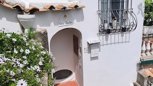 Um edifício branco com telhado em telhas, uma janela com grades metálicas e uma pequena varanda.