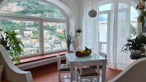 Quarto com teto alto abobadado, mesa de jantar com cadeiras, sofá com almofadas e vista para a cidade através de janelas amplas.