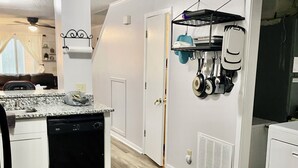 A compact kitchen with a dishwasher, a sink, and a countertop. There is a door leading to another room, and a wall-mounted rack holding kitchen utensils. - Beautiful & Stylish 2 BR & 2.5 Baths 10min downtown, 5min Lexington Med Center (Columbia)