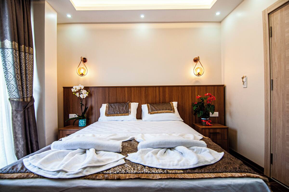 A neatly made bed with white linens, two bedside tables with lamps, and a wooden headboard.