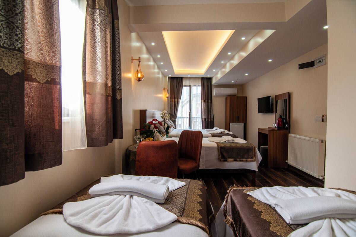 A hotel room with two beds, a sitting area with a chair, a TV, and a small table with a kettle.