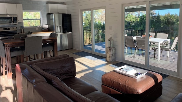 Eine moderne Küche mit Kühlschrank, Mikrowelle und Backofen. Es gibt einen Essbereich mit Tisch und Stühlen sowie ein großes Fenster mit Blick auf eine Terrasse.