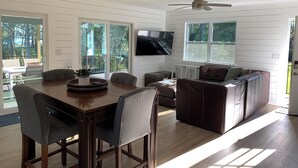 Ein modernes Wohnzimmer mit einem Holzesstisch, grau gepolsterten Stühlen, einem braunen Ledersofa und einem Deckenventilator.
