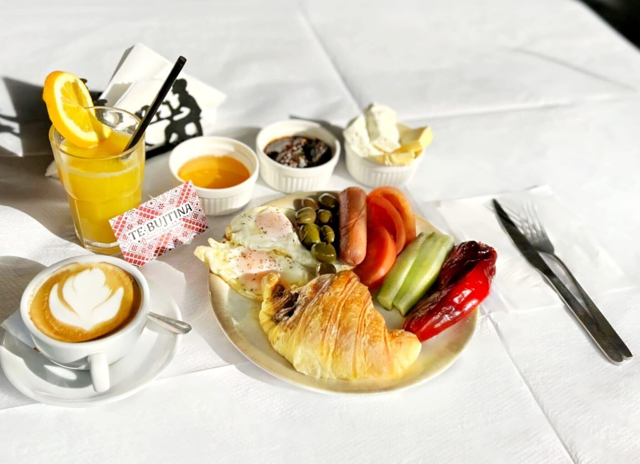 Une assiette de petit-déjeuner avec des œufs, un croissant, des tomates, des concombres et des poivrons, un verre de jus d’orange et une tasse de café.