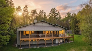 A two-story cabin with a deck, surrounded by forest. - Waterfront w/ Kayaks, Paddleboards and a Hot Tub (Tupper Lake)