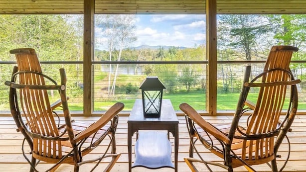 A wooden deck with two rocking chairs and a table with a lantern. - Waterfront w/ Kayaks, Paddleboards and a Hot Tub (Tupper Lake)