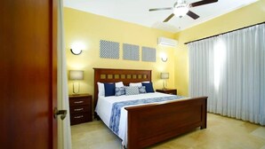 A bedroom with a wooden bed, two bedside tables, a ceiling fan, and a window with curtains. - 8 Bedroom Private Property (Sosua)