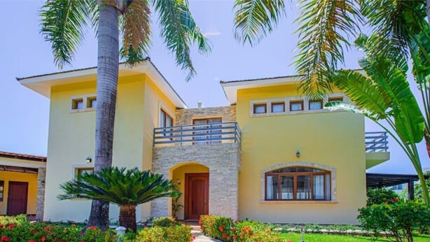 A two-story building with a stone entrance, a balcony, and a well-maintained garden with red flowers and palm trees. - 8 Bedroom Private Property (Sosua)
