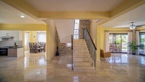 A spacious living area with a staircase leading to a balcony, a kitchen with white cabinets, and a dining area with chairs. - 8 Bedroom Private Property (Sosua)