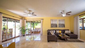 A spacious living room with a large sofa set, two ceiling fans, and a view through the glass doors to an outdoor patio area. - 8 Bedroom Private Property (Sosua)