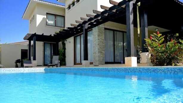 Ein modernes Haus mit Schwimmbad, überdachter Terrasse und einem Garten mit Pflanzen.