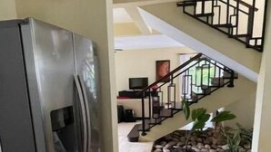 Eine Küche mit einem Edelstahl-Kühlschrank, einer Treppe, die in einen Wohnbereich mit Fernseher führt, und einem kleinen Innenhof.