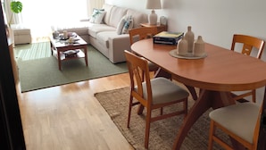 Ett modernt vardagsrum med en soffa, ett matbord med stolar, ett soffbord, en lampa och en kristallkrona.