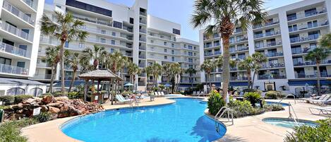 A hotel pool area with multiple lounge chairs, palm trees, and a large swimming pool.