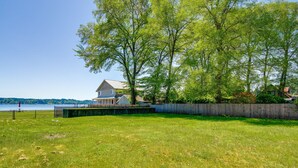 A grassy area with a wooden fence, a house, and a body of water in the background. - Waterfront Hood Canal Cottage: Steps to the Beach! (Belfair)