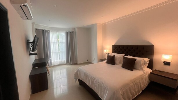 A hotel room with a large bed, two bedside tables with lamps, a flat-screen TV mounted on the wall, and a window with curtains. - Hotel Zuriel Boutique (Cartagena)