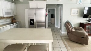 Une cuisine moderne avec des meubles blancs, un réfrigérateur en acier inoxydable et un coin repas comprenant une table et des chaises.