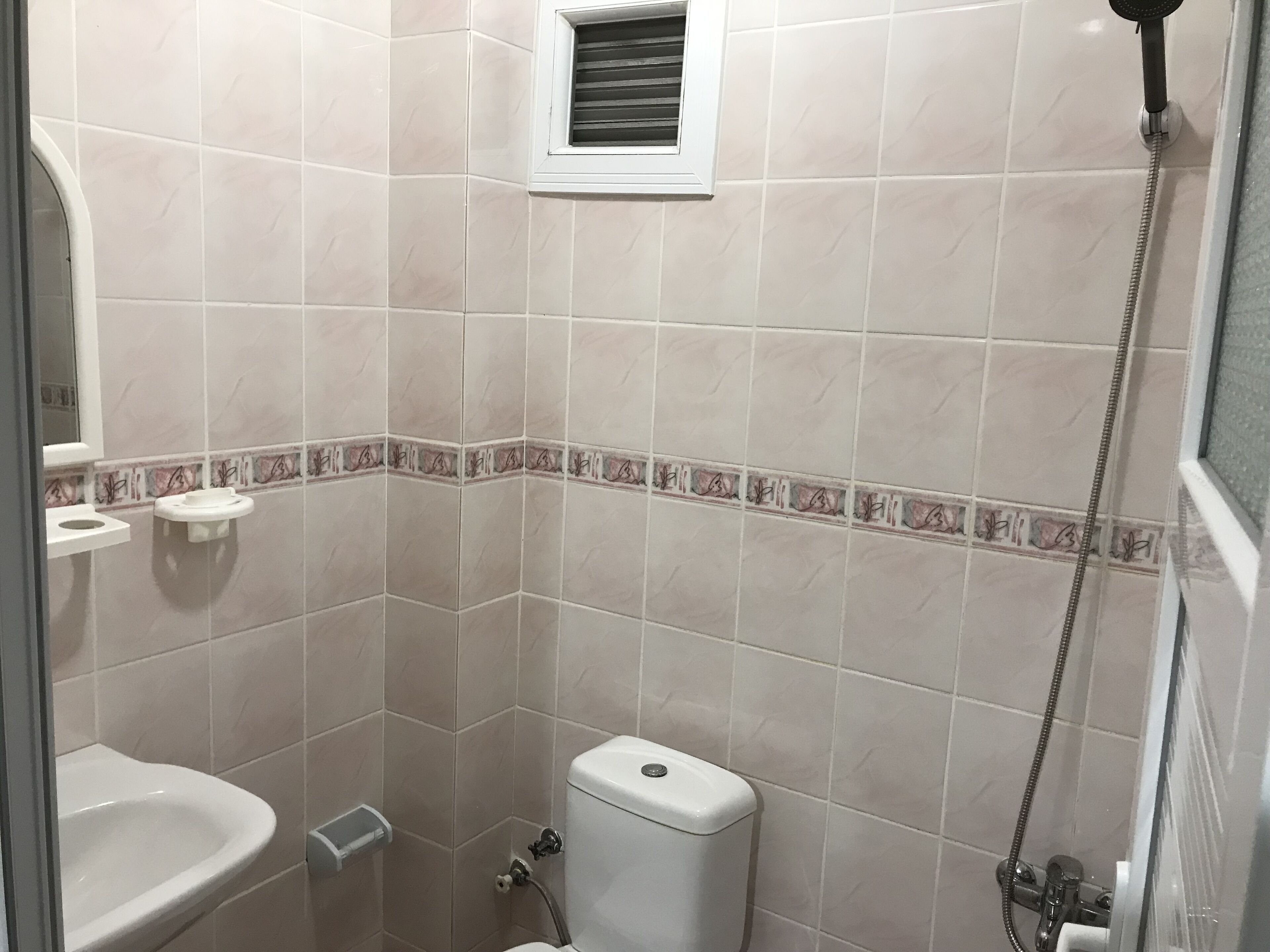 A bathroom with a toilet, sink, shower, and a small window.