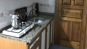 A compact kitchen with wooden cabinets, a granite countertop, a gas stove, a sink, and a door with a decorative metal handle. - Joey Pansiyon (Marmara)