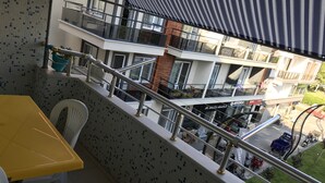 Un balcon avec une table et des chaises jaunes, un mur recouvert de carreaux et une vue sur un immeuble à plusieurs étages, doté de balcons et de boutiques.