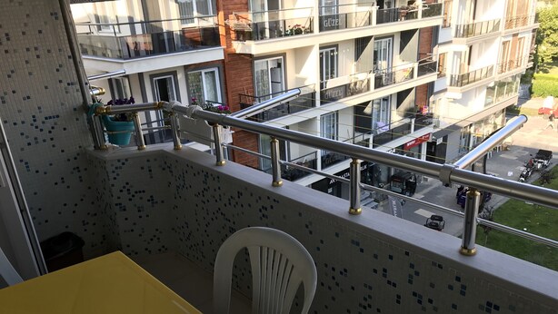 Un balcon avec une table jaune et une chaise blanche, donnant sur un immeuble à plusieurs étages doté de balcons et offrant une vue sur la rue.
