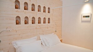 Quarto com cabeceira de madeira com vários recortes em arco, cama com roupa de cama branca e uma pequena mesa de cabeceira.